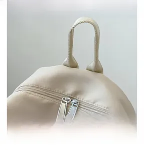 Close-up of nylon backpack with dual metal zippers and brown leather pulls on top