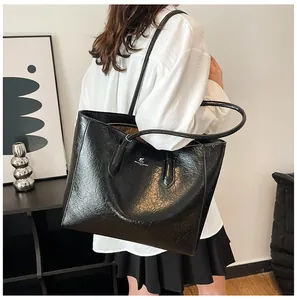 Modern black tote bag in textured faux leather worn by a model in a minimalist setting