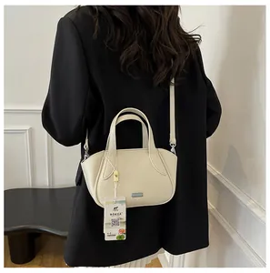 Detailansicht der cremefarbenen Ledertasche mit Litschi-Textur, getragen von einem Model