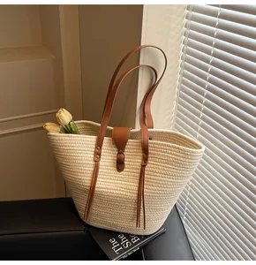 Close-up of woven tote bag with brown leather straps, tassel details and buckle closure