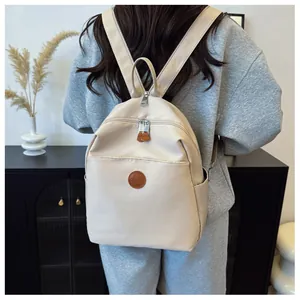 Close-up of beige nylon backpack with silver zippers and brown leather logo patch details