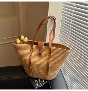 Detail of straw woven tote bag featuring brown leather straps and buckle in natural light