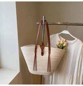 Detail of a straw woven tote bag featuring dark brown leather straps and elegant tassels