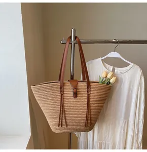 Detail of woven straw tote bag featuring brown leather handles and decorative tassel