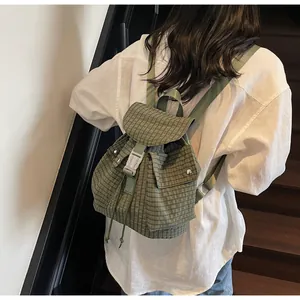 Top view of green plaid canvas backpack detail showing buckle closure and drawstring design