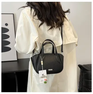 Modische schwarze Lederhandtasche, getragen von Model im weißen Mantel vor Kunsthintergrund