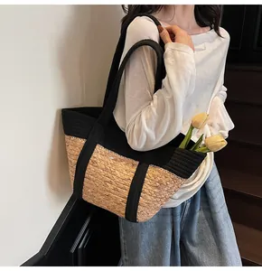 Detail of a large capacity two-tone straw tote bag featuring black fabric shoulder straps