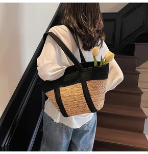 Detail view of woven straw tote bag with black strap worn on shoulder by female model