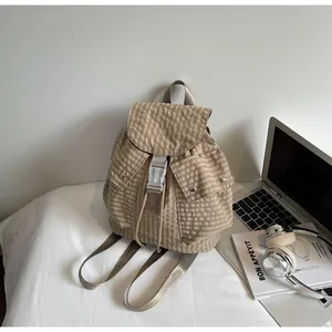 Detail of beige gingham backpack with plastic buckles on a bed near a laptop