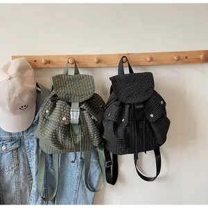 Detail of plaid canvas backpacks in green and black with drawstring and buckle closure