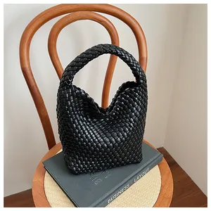 Gros plan d'un sac hobo tressé noir posé sur un livre dans un intérieur au style minimaliste