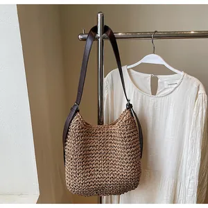 Detail of hand-woven straw shoulder bag with adjustable leather strap on silver rack