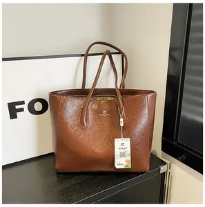 Close-up of brown glossy leather tote bag showing fine oily texture and silver logo