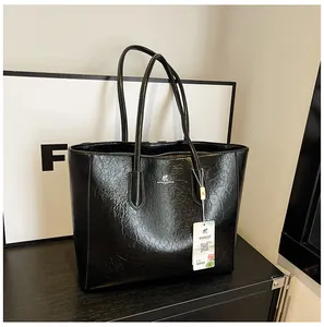 Macro detail of black crinkled patent leather tote bag showing texture and logo