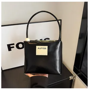Dettaglio di una borsa quadrata nera chic con perla grande e applicazione logo bianca