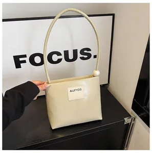 Dettaglio della borsa squadrata color crema con una grande perla sul manico lungo