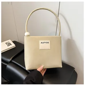 Dettaglio di borsa squadrata beige con grande manico rotondo e dettaglio in perla bianca