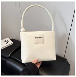 Dettaglio borsa in pelle bianco crema con manico singolo e ornamento a sfera sul divano