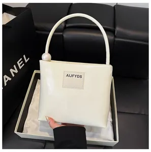 Dettaglio borsa in pelle crema con una grande perla decorativa sul manico arrotondato