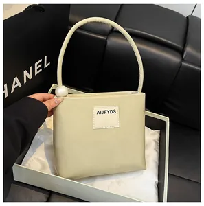 Dettaglio di borsa squadrata beige con accento di perle e logo dal design minimale