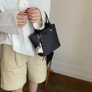 Black litchi grain bucket bag with baseball charm, minimalist tote shown by model