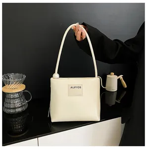 Dettaglio della borsa in pelle color crema con grande perla e etichetta con logo