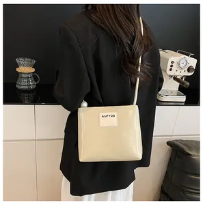 Dettaglio borsa quadrata in pelle beige con perla sulla tracolla e toppa con logo brand
