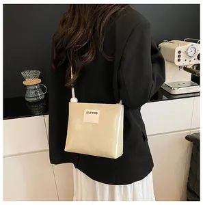 Dettaglio borsa in pelle crema con patch di lettere e grandi perle decorative sulla tracolla