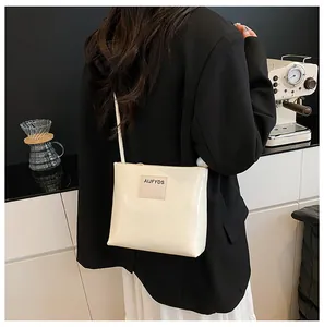 Dettaglio di una borsa a tracolla quadrata crema con logo AIJFYDS in un ambiente cafè