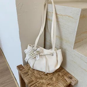 Nahaufnahme der cremefarbenen Ledertasche mit Perlenherz und Schleifenanhänger Detail