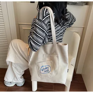 Detail of minimalist cream canvas tote bag with blue #today midi embroidery and front pockets