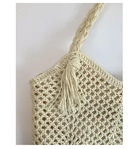 Close-up of the hollow crochet texture and tassel detail on this beige woven tote bag