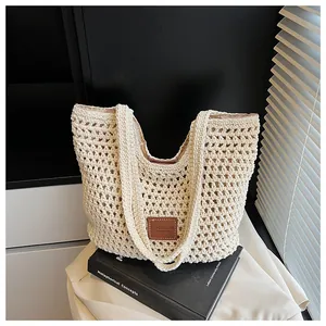 Dettaglio di una borsa tote in maglia crema con etichetta in pelle marrone sopra un libro