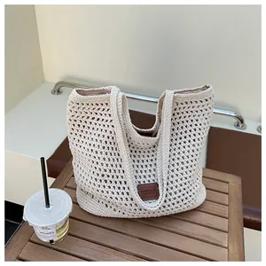 Dettaglio borsa tote intrecciata beige con patch in pelle su tavolo in legno con bibita