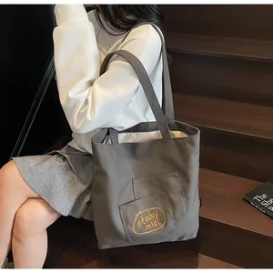 Detail view of grey canvas tote bag with yellow embroidery and front pocket on stairs