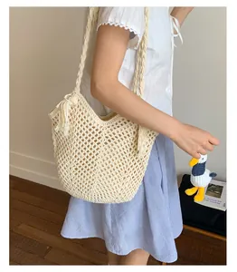 Close-up of handmade hollow crochet tote bag with fringe details and cute plush pendant