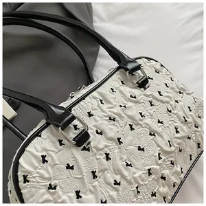 Detail of white pleated handbag featuring black cross embroidery and leather handles