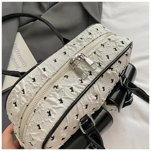 Top view of textured white handbag featuring black bow patterns and silver metal zippers