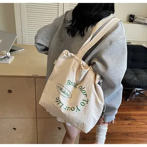 Detailed view of cream canvas tote bag with green lettering and adjustable strap