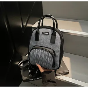 Close-up of mini grey denim fabric and black leather backpack with wavy pleats and brand plaque
