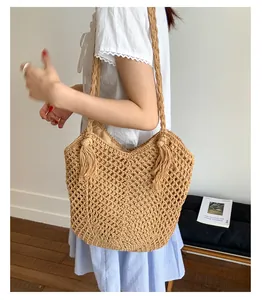 Detail of woven straw tote bag with intricate hollow mesh patterns and large decorative tassels