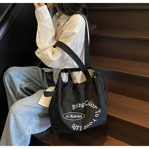 Detail of black nylon tote bag with drawstring closure and white artistic typography