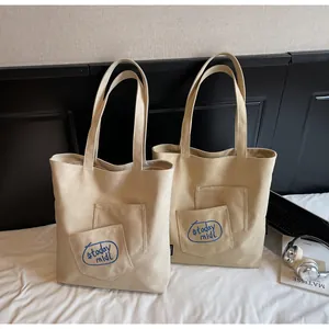 Close-up of beige canvas tote bag showing double pockets and blue embroidered logo