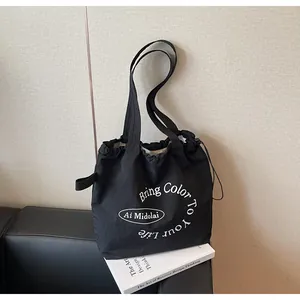 Detail of black canvas tote bag with drawstring closure and white letter print