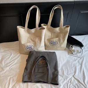 Three minimalist canvas tote bags in white, khaki, and grey with external pockets