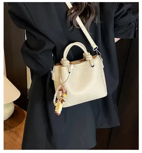 Detalle de bolso blanco crema con textura de lichi, colgante de perlas y logo de moda
