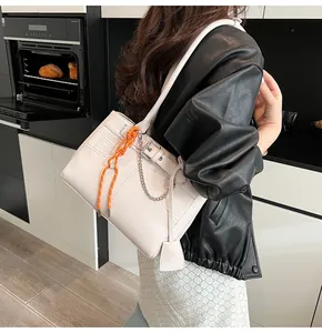 Dettaglio borsa tote color crema con nodo arancione e catena d'argento in ambiente moderno