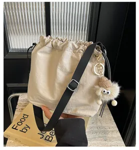 Détail du sac seau beige à cordon avec bandoulière noire et pendentif en peluche