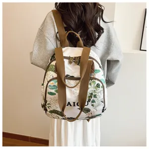 Detail shot of white canvas backpack with green floral print and brown woven straps