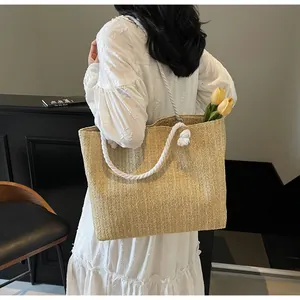 Detail view of woven straw tote bag featuring thick white cotton rope handles and knot accents